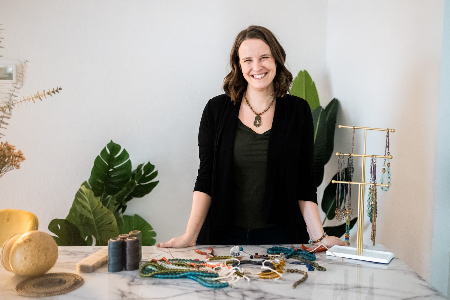 Angel standing at desk with beads on table and jewelry.